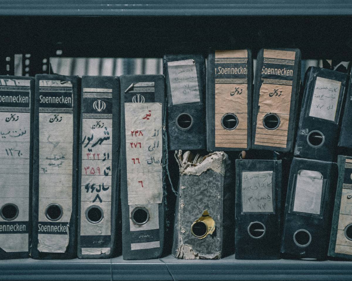 A row of old, worn binders on a dusty shelf.