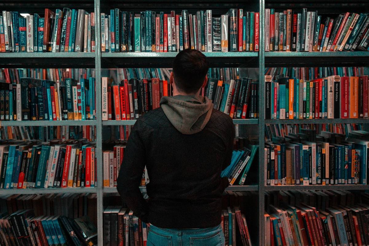 person wearing black and gray jacket in front of bookshelf